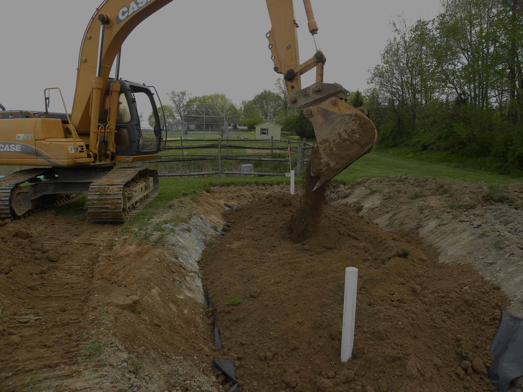 Large backhoe filling a dirt hole at job site